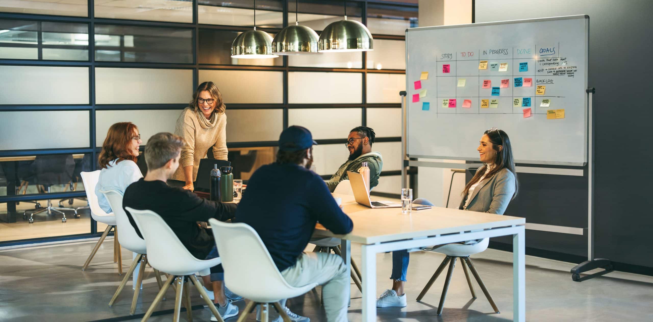Successful teamwork in a diverse office: Colleagues smiling and talking in a productive meeting weibliche Führungskraft, die sich freundlich an ihr Team wendet.